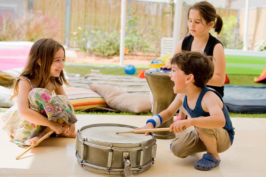 Three children joyfully playing drums in a backyard, exploring the joy of music together