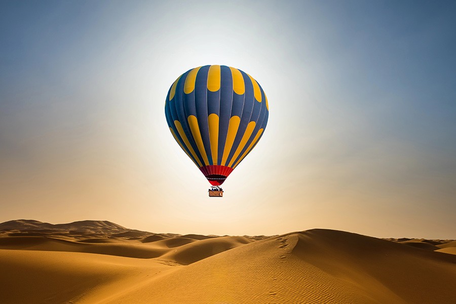 A vibrant hot air balloon soars over the vast desert, showcasing Dubai's thrilling adventures below