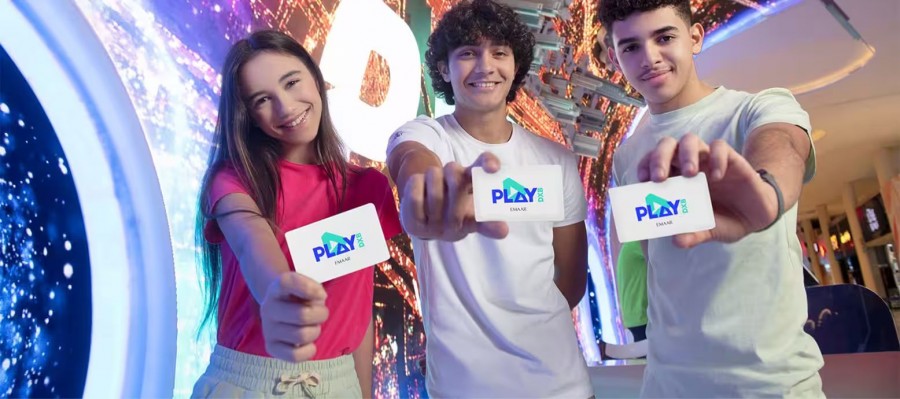 Three young people excitedly hold up cards displaying the Play DXB logo at a fun event in Dubai