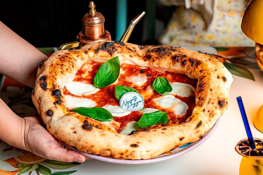 A person proudly displays a basil-topped pizza, highlighting a delightful choice for families at family friendly restaurants in Dubai