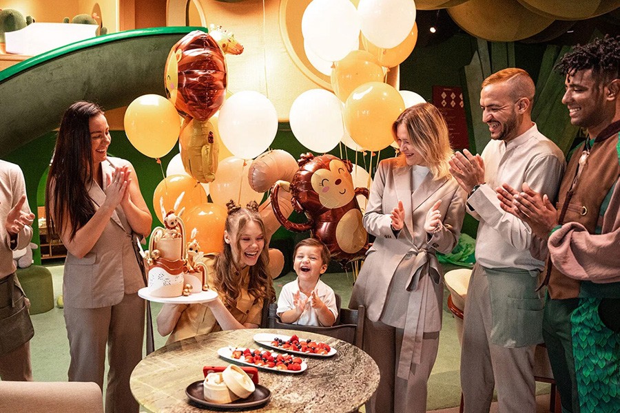 A cheerful group of people celebrating with a colorful cake and balloons at a Family friendly restaurant in Dubai