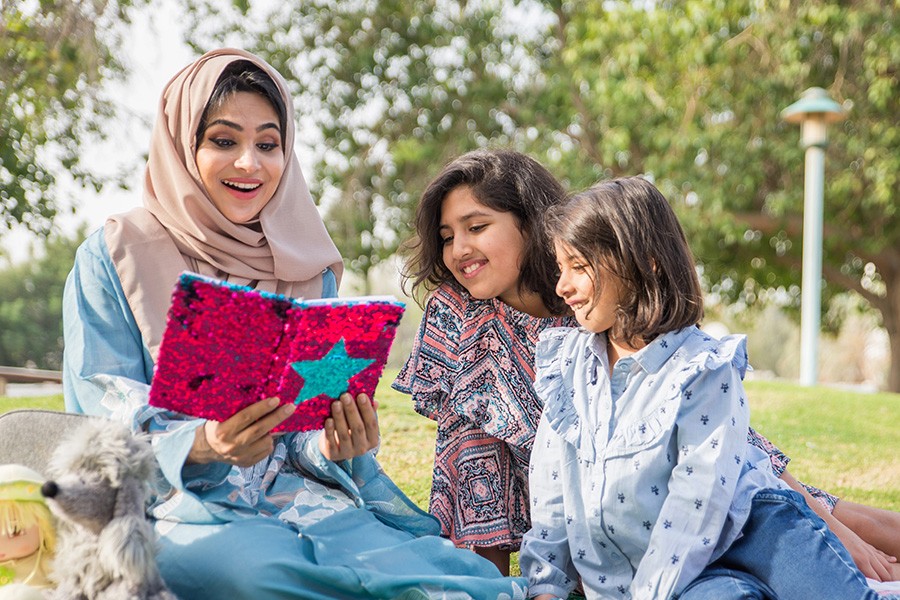 A woman and two children reading a book best things to do with Kids