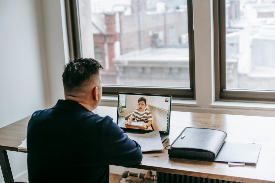 A man at a desk with a laptop, engaged in a video call, tutoring children online