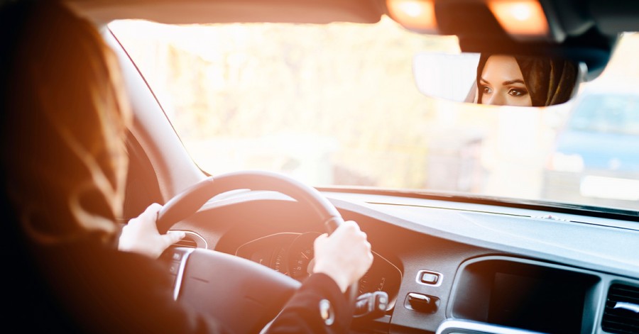 A woman happily driving a car with the sun setting behind her