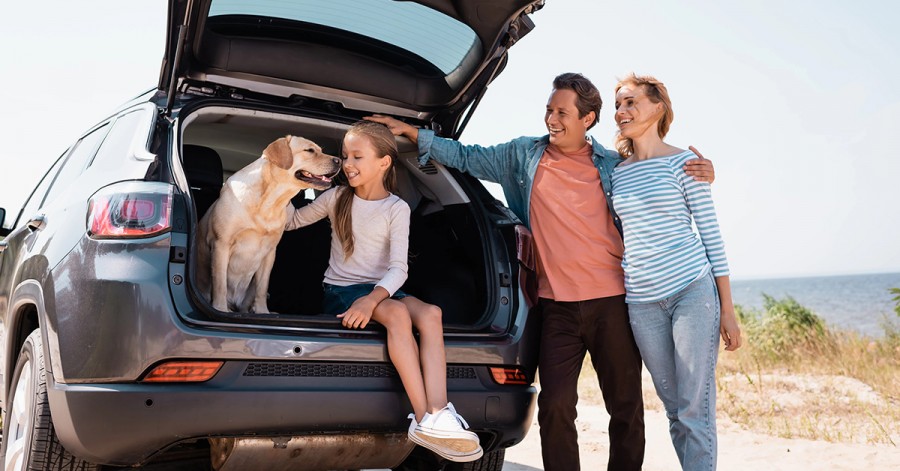 A cheerful family and their dog are in the trunk of a car, excited for a road trip exploring Dubai's attractions