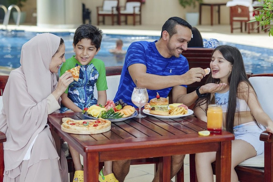A family enjoying pizza and juice by the pool at Millennium Best Family Friendly Hotels in Dubai