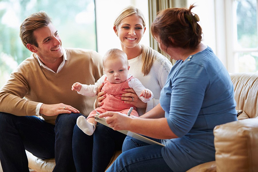 A family sits together on a couch, with a smiling baby in the mother's arms