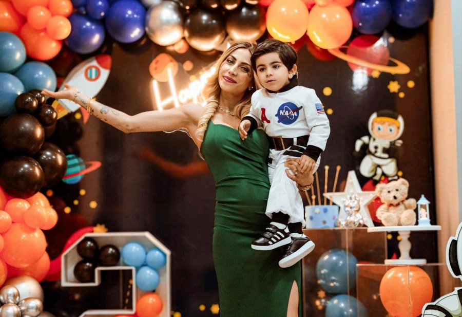 A woman and child in colorful space costumes smile for a photo at a birthday party, surrounded by festive decorations