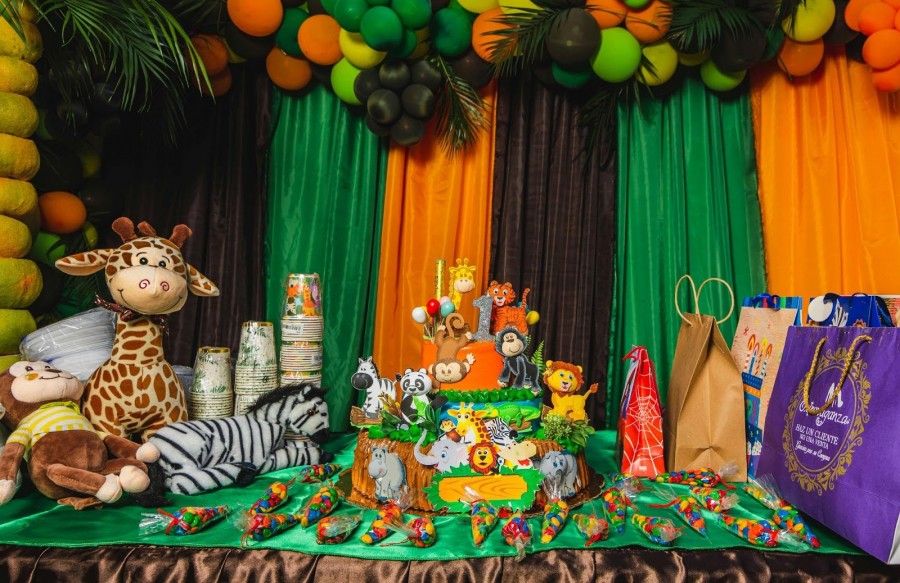 A vibrant jungle-themed birthday party featuring a colorful cake, balloons, and various stuffed animals