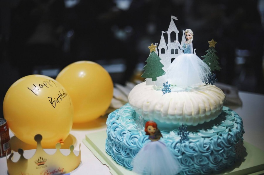 A colorful birthday cake topped with a princess figurine, set against a festive party backdrop
