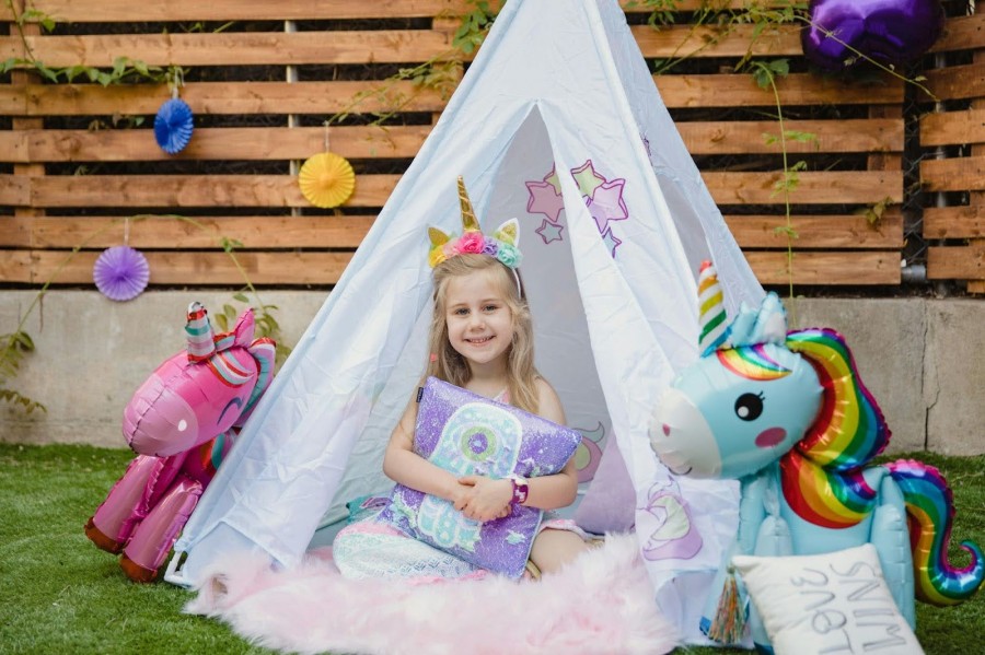 A little girl joyfully sitting inside a colorful unicorn tent at her birthday party, surrounded by festive decorations
