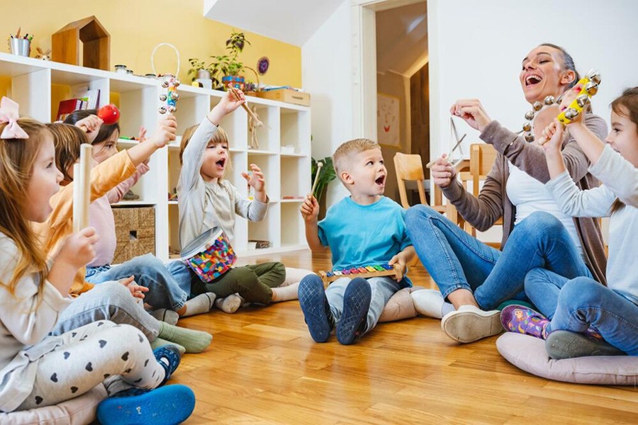 Children sitting on the floor with their hands raised, expressing excitement and engagement in a group activity.