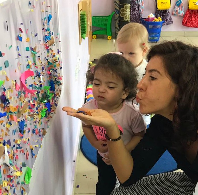 A woman and two children observe a wall adorned with vibrant confetti in a Dubai nursery setting