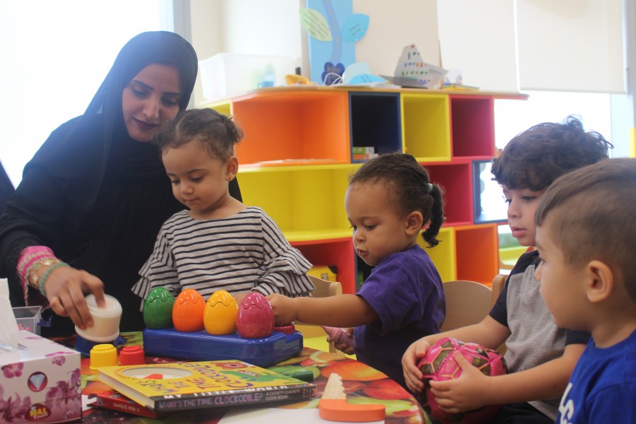 A woman and children joyfully playing with toys in a Dubai Babilou Nursery classroom